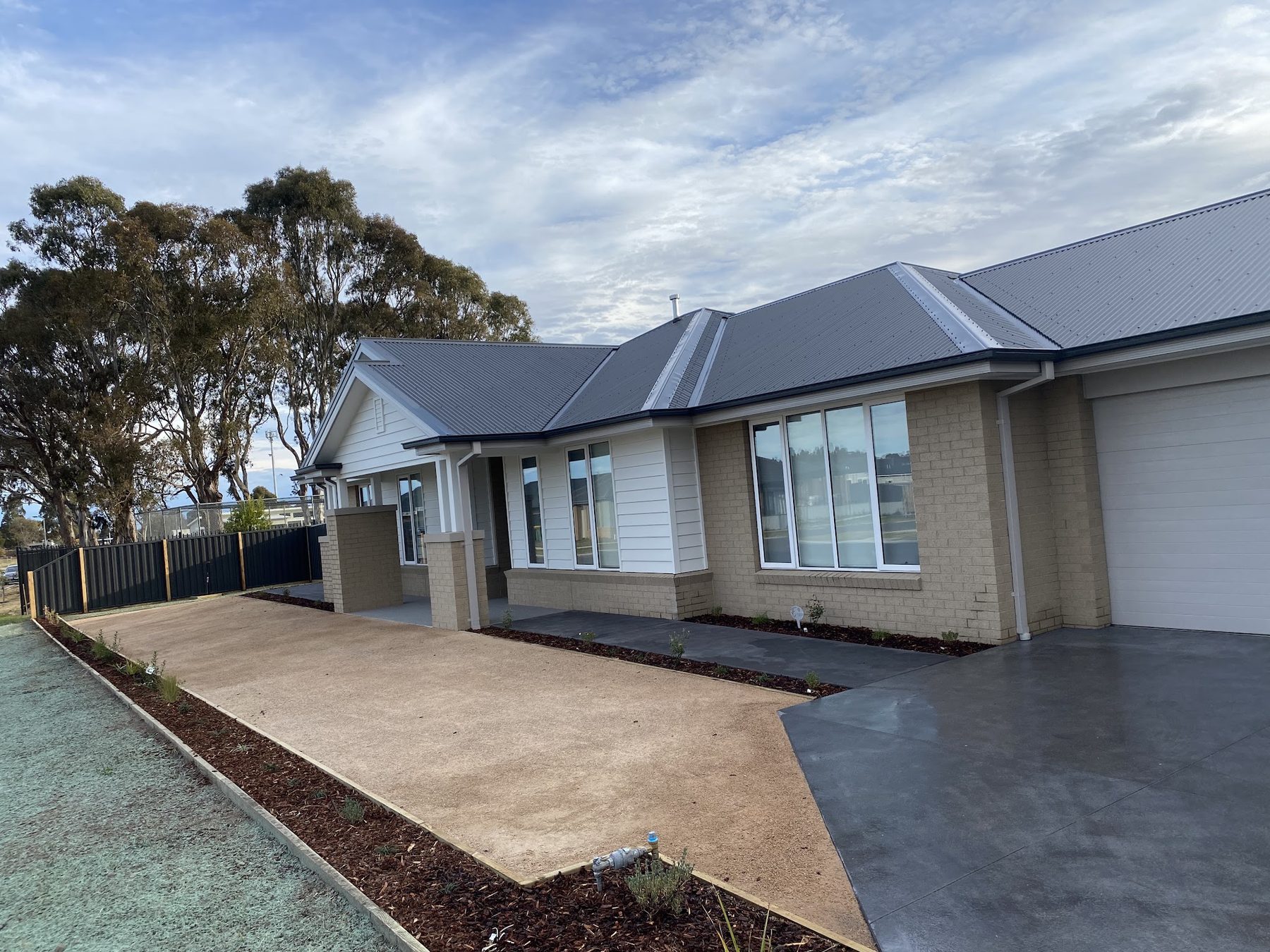 A new home frontage with an exposed aggregate driveway, mulched garden beds and fresh plantings along the path