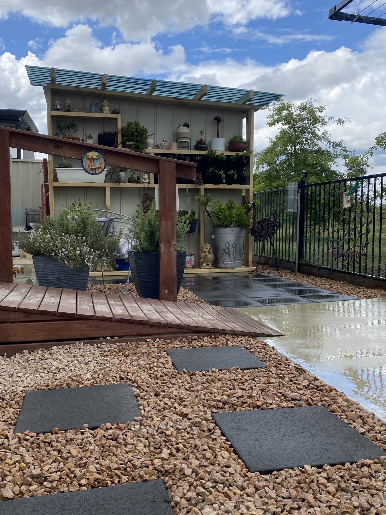 A curved hardwood boardwalk beside a timber plant display shelf, with gravel and charcoal stepping pavers