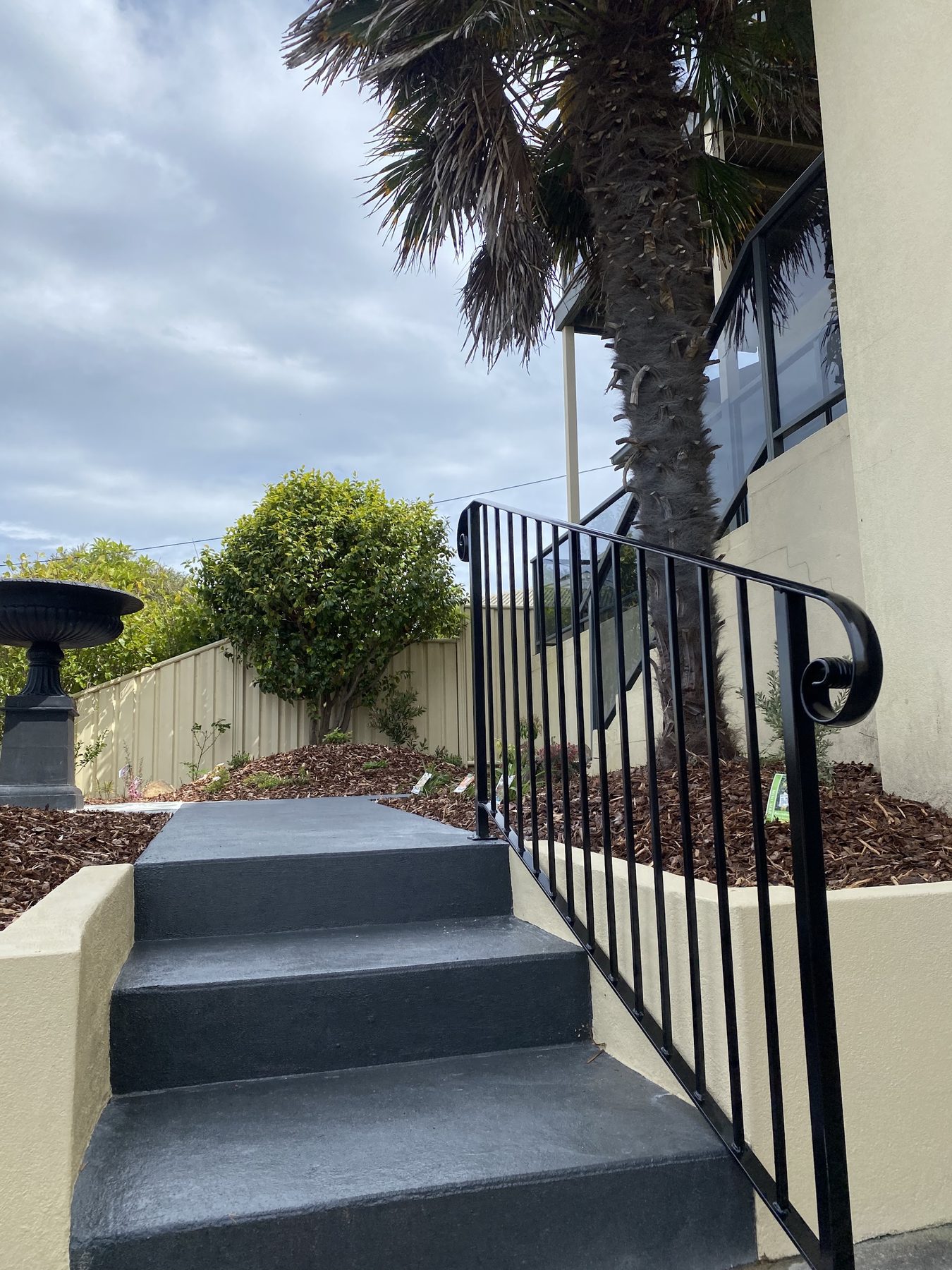 A front garden with rendered garden walls, painted concrete steps, a wrought iron handrail and mulched beds