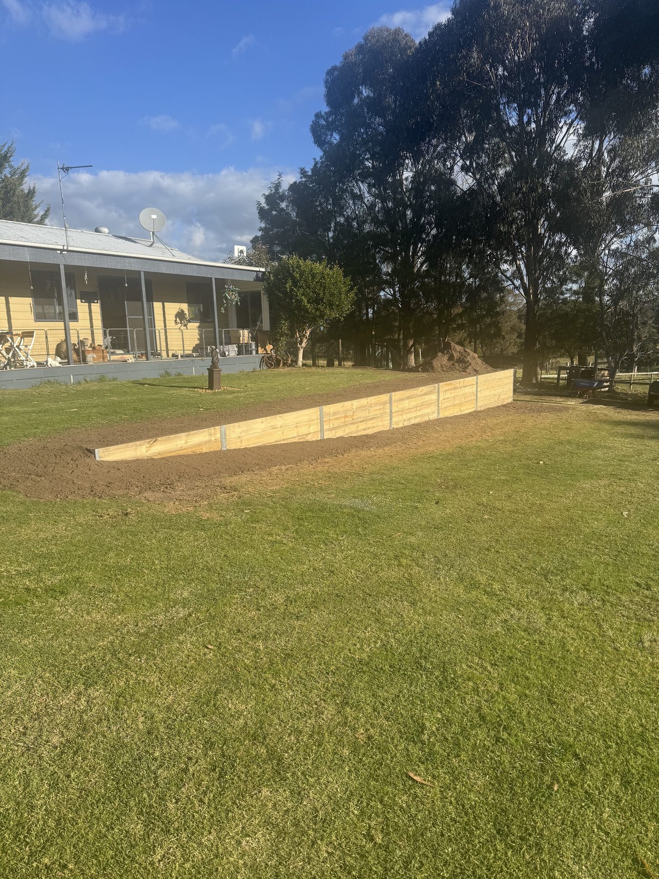 A long treated pine sleeper retaining wall newly built across a rural property, with the ground graded behind it